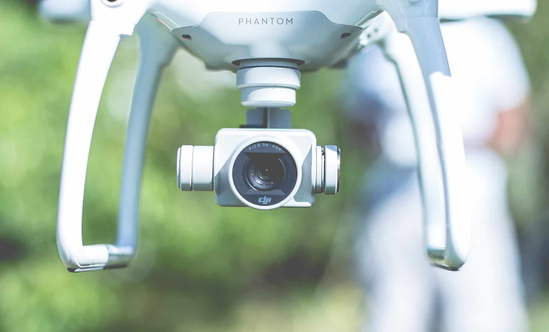Close-up of a white drone camera, with blurred green background.